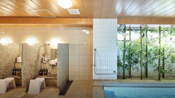 A modern bathroom with a shower, toilet, and sink, a pool area with bamboo plants, and a ceiling with wooden panels and recessed lighting.