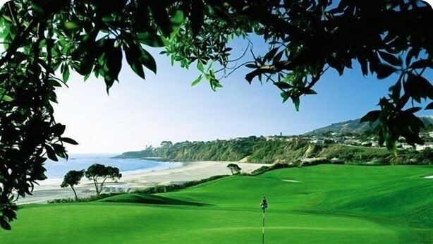 A golf course with a flagstick, trees, and a view of the ocean and hills in the background. - BEAUTIFUL, LUXURY CONDO, GATED WITH WALKING TRAIL TO BEACH! (Dana Point)