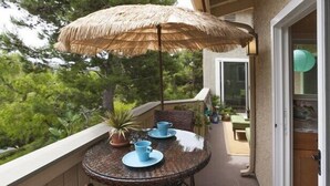 A balcony with a wicker table, blue cups, a potted plant, and a thatched umbrella. - BEAUTIFUL, LUXURY CONDO, GATED WITH WALKING TRAIL TO BEACH! (Dana Point)