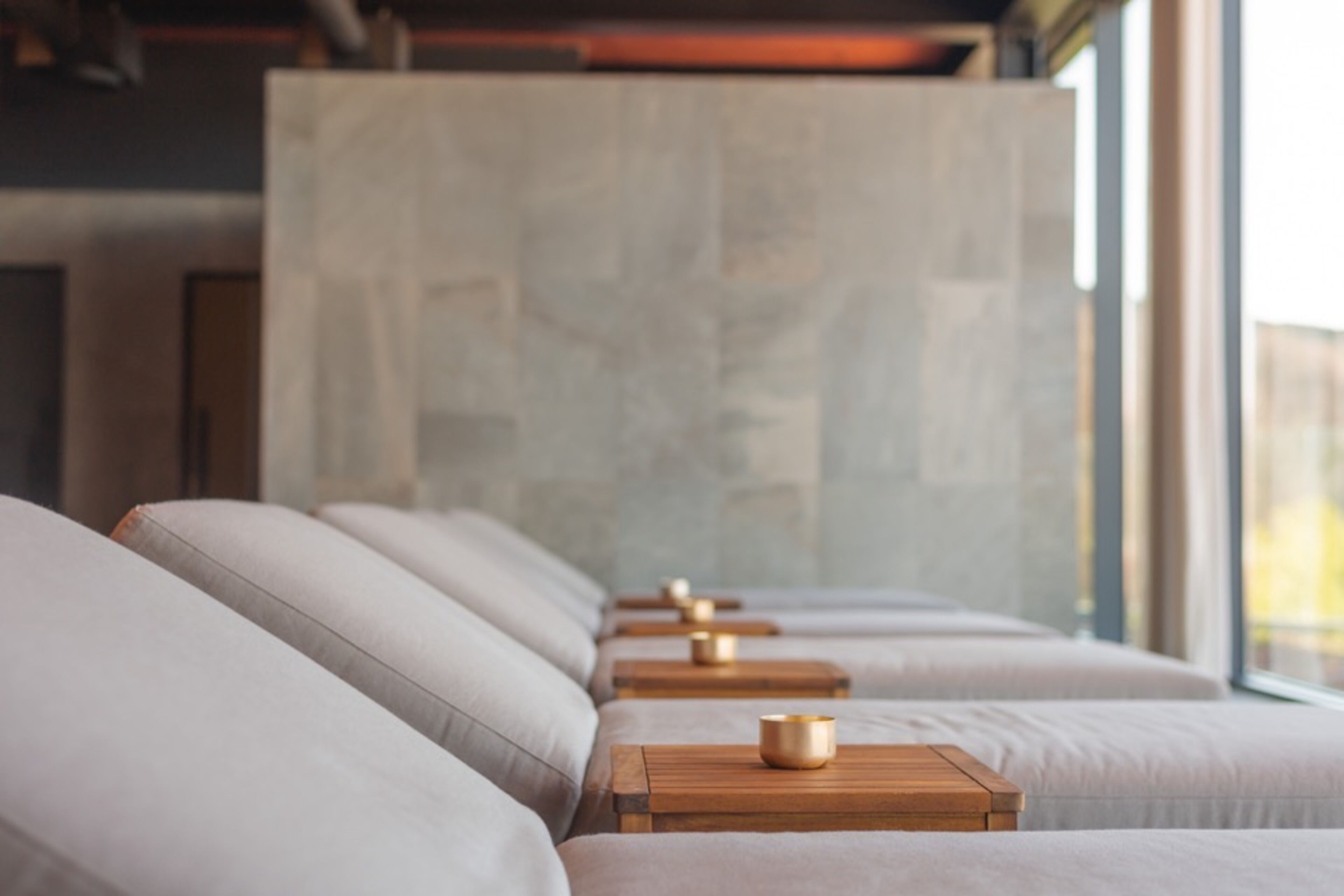 A row of cushioned seating with wooden side tables, each with a small object on top.