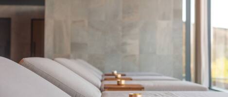 A row of cushioned seating with wooden side tables, each with a small object on top.