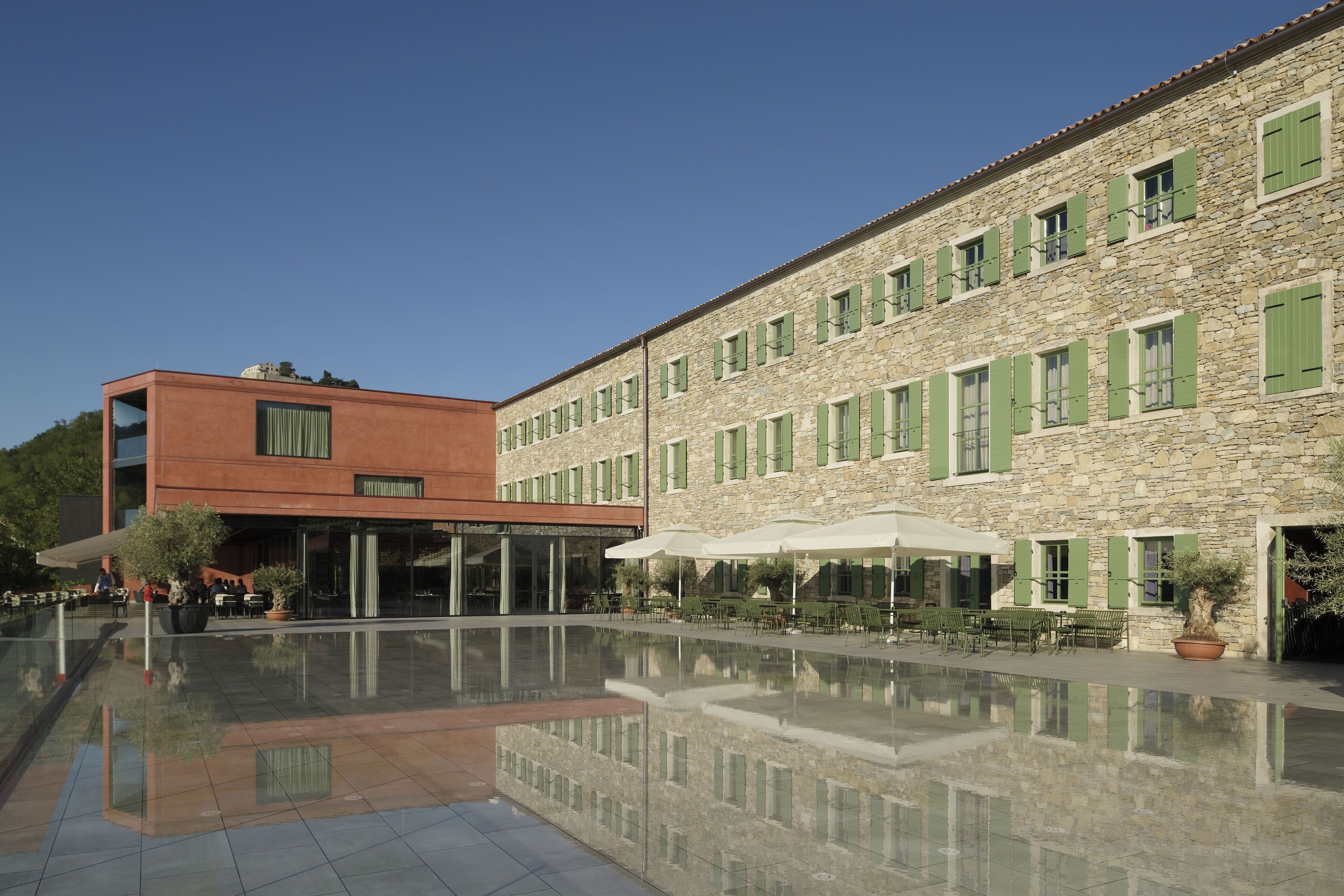 Un patio con un edificio moderno y otro de piedra con contraventanas verdes.