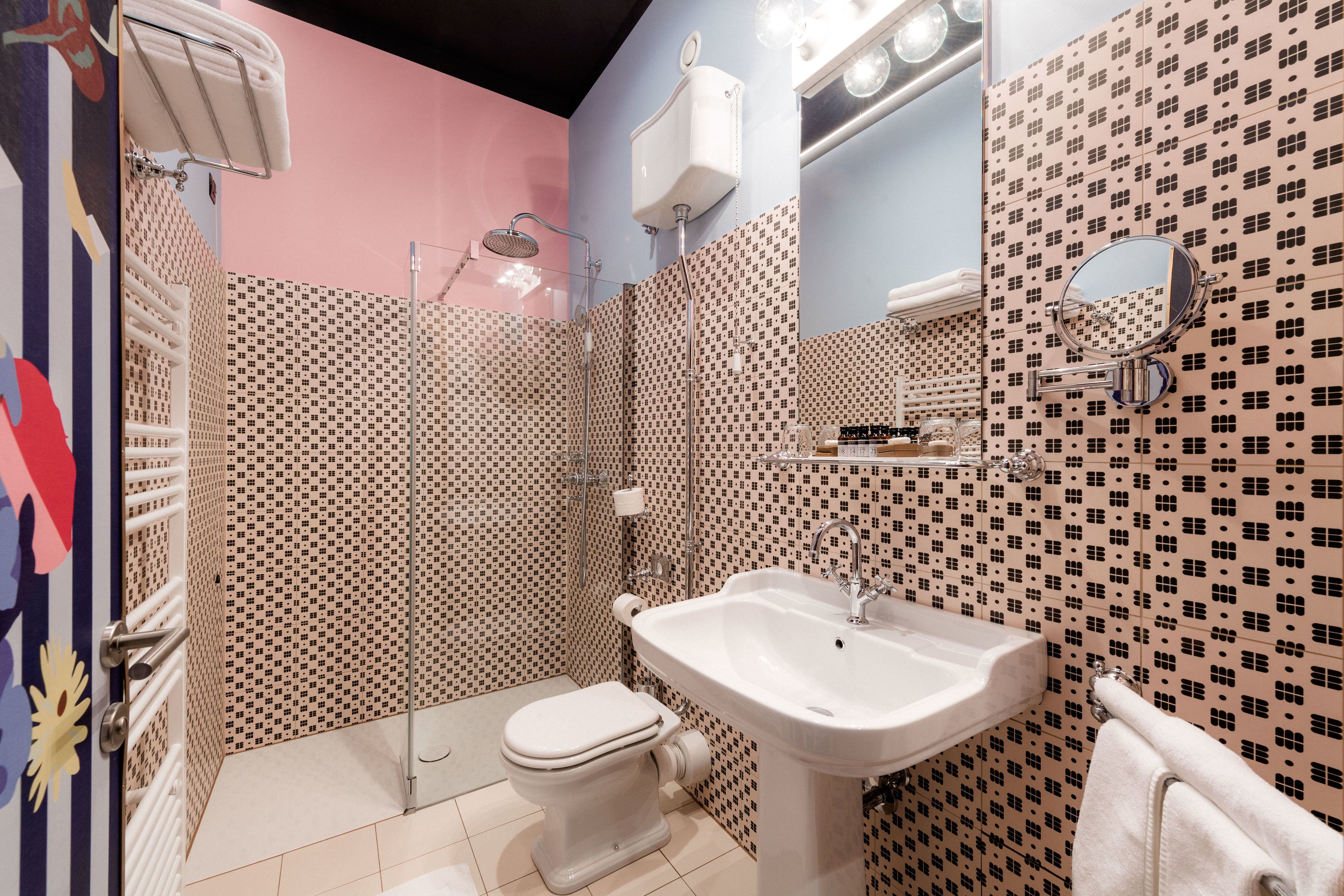 A bathroom with a shower, toilet, and sink, featuring patterned tiles and a mirror.