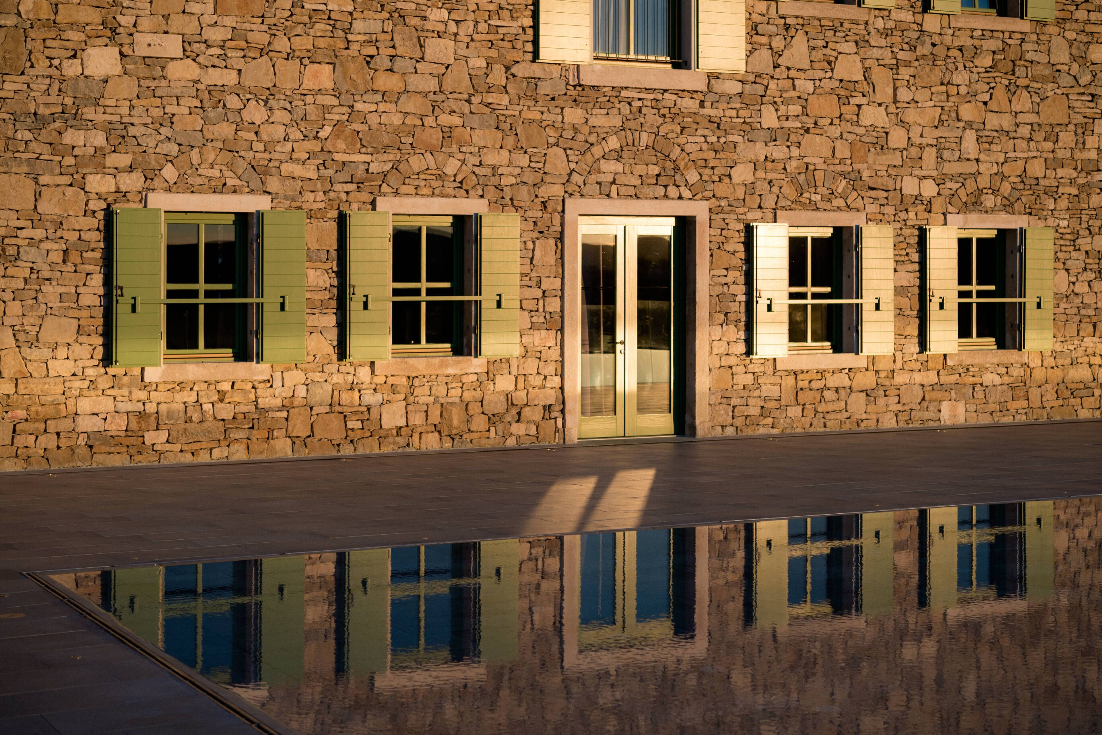 Un edificio de piedra con varias ventanas y puertas, reflejado en un estanque.