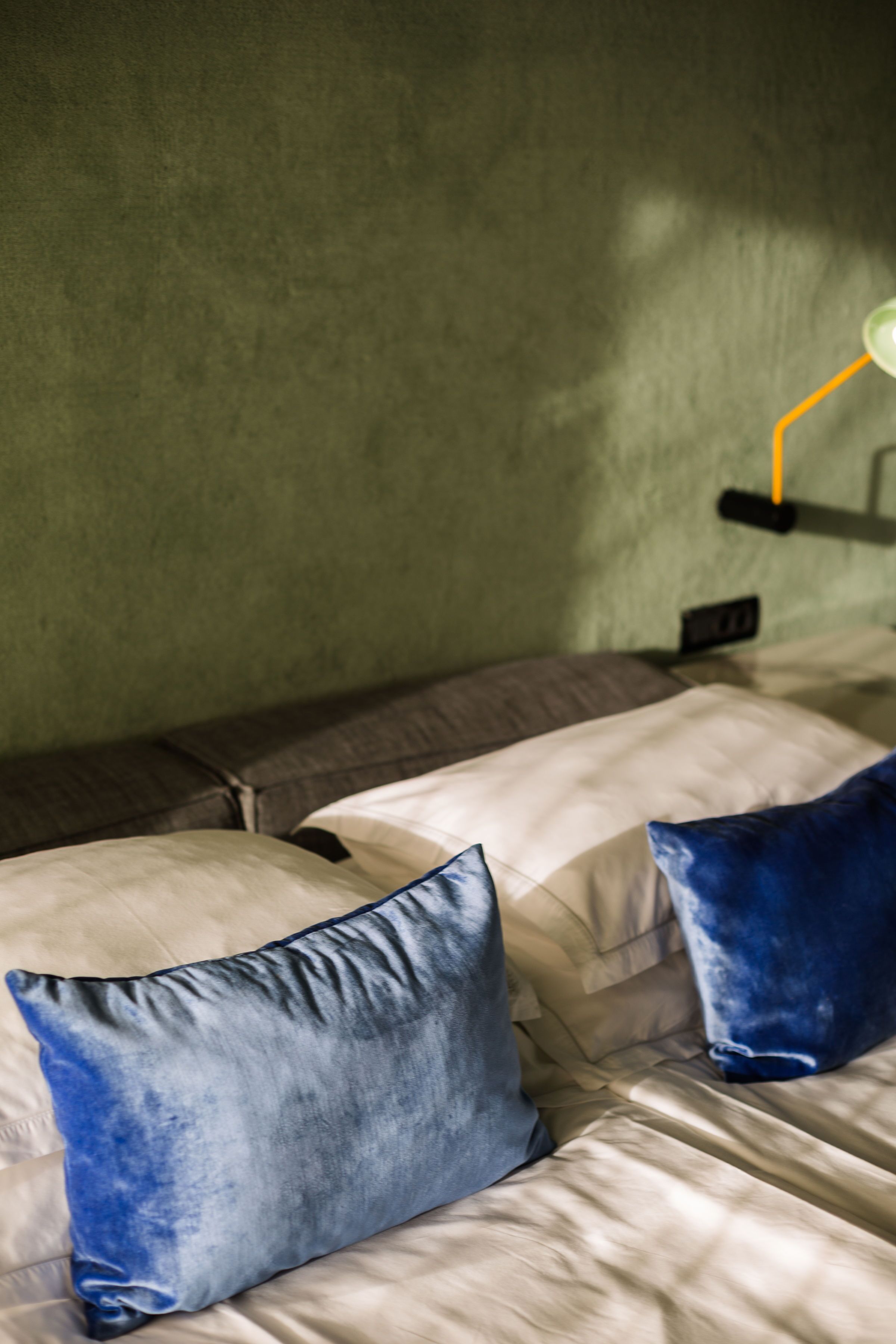 Una cama con un almohadón blanco y azul, un almohadón marrón y una lámpara en una mesita de noche.