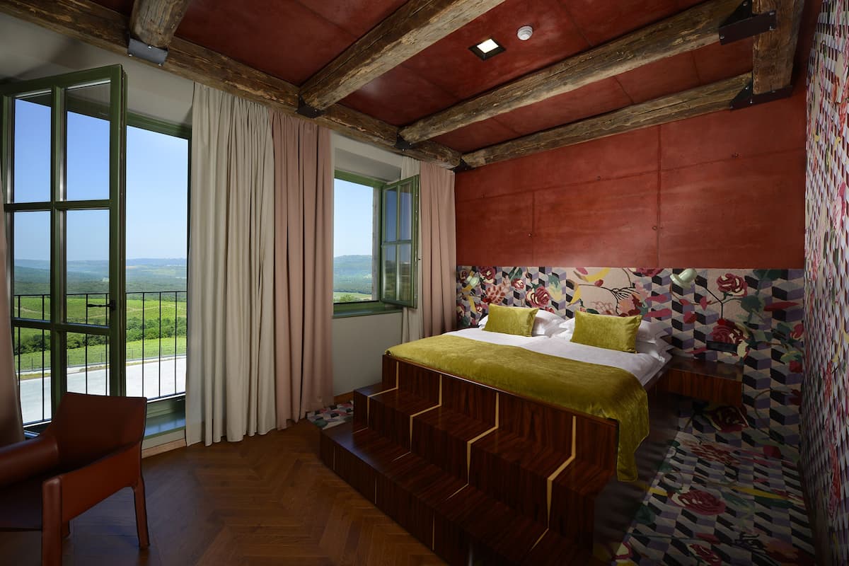 A bedroom with a bed, a chair, and a view of the outdoors.