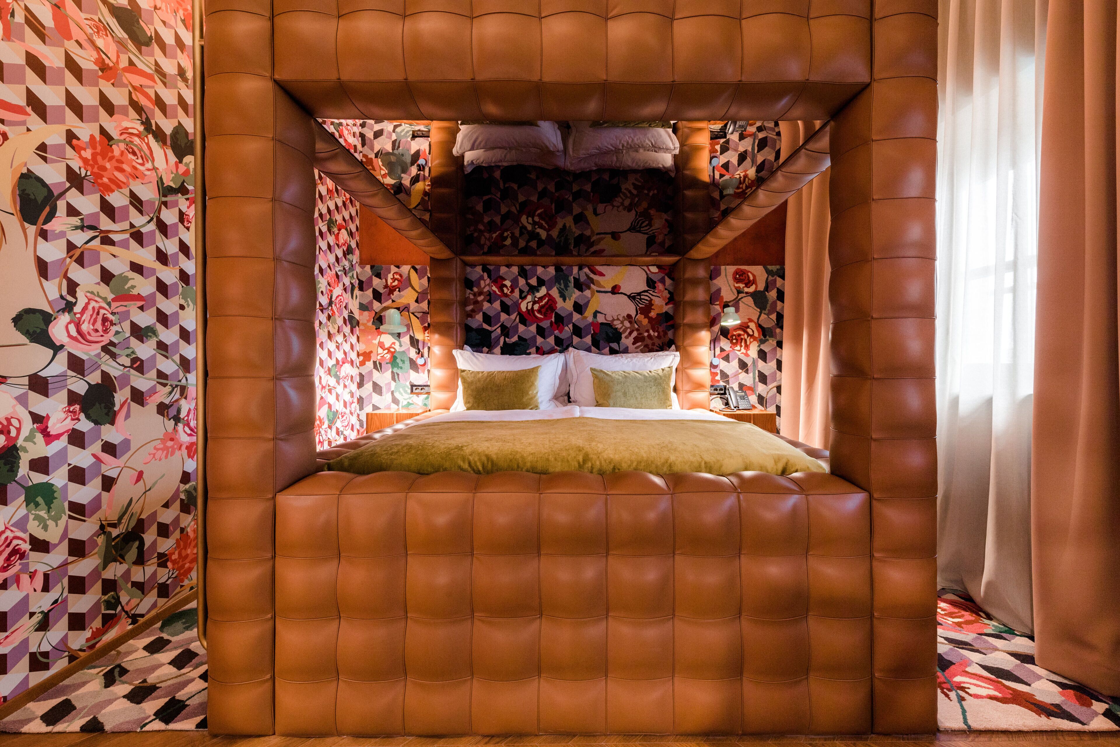 A uniquely designed room with a geometric patterned wall, a tufted leather headboard, and a patterned rug.
