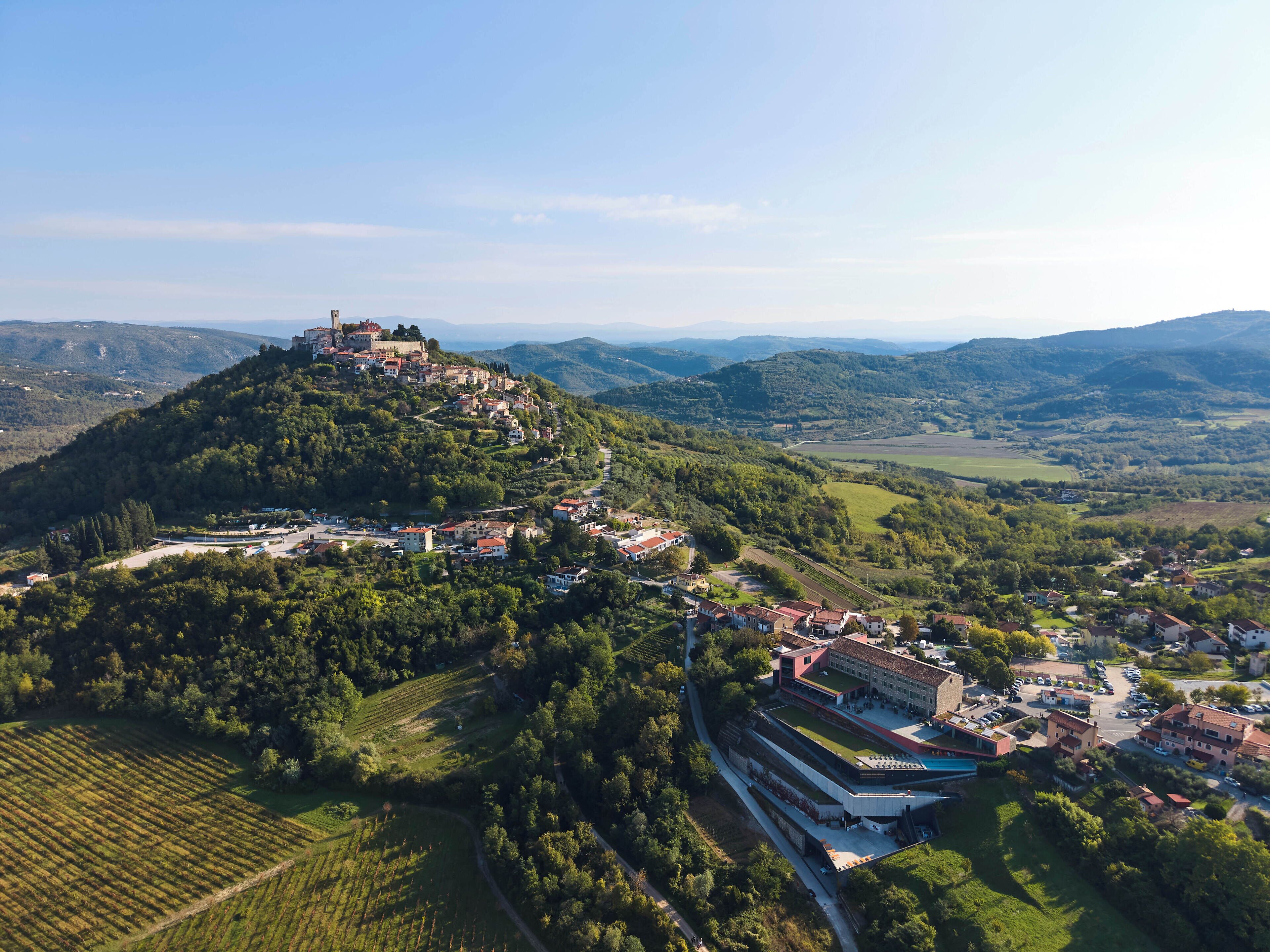 An aerial view of a town with a castle on a hill, surrounded by green fields and residential buildings.