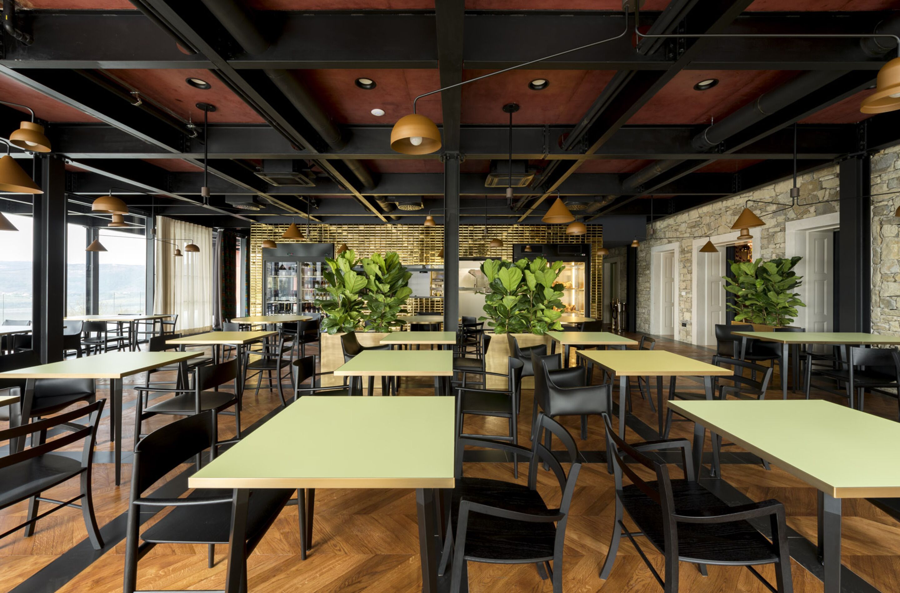 A modern restaurant with high ceilings, exposed beams, and large windows offering views. Tables are arranged in a spacious layout with chairs.