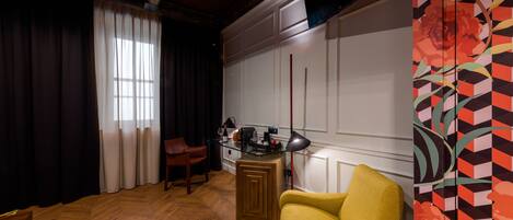 A room with a wooden herringbone floor, a yellow armchair, a glass-top coffee table, a red lamp, and a decorative panel with a geometric floral pattern.