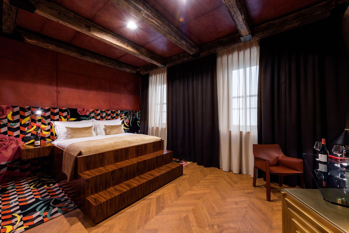 A bedroom with a wooden bed, a chair, and a glass table with wine bottles.