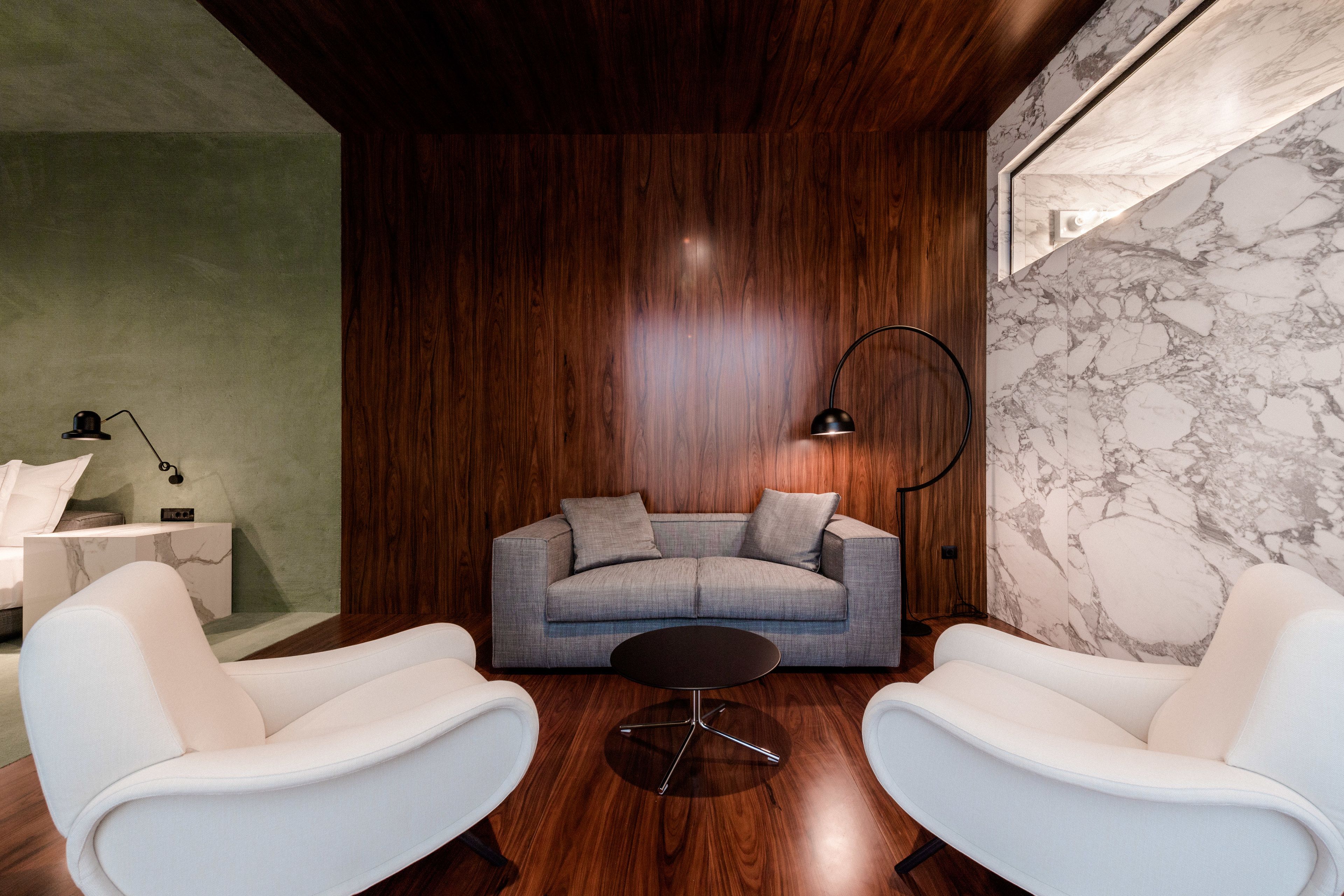 A modern living room with a grey sofa, two white armchairs, a round coffee table, and a marble wall.