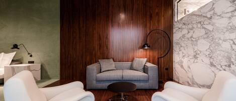 A modern living room with a grey sofa, two white armchairs, a round coffee table, and a marble wall.