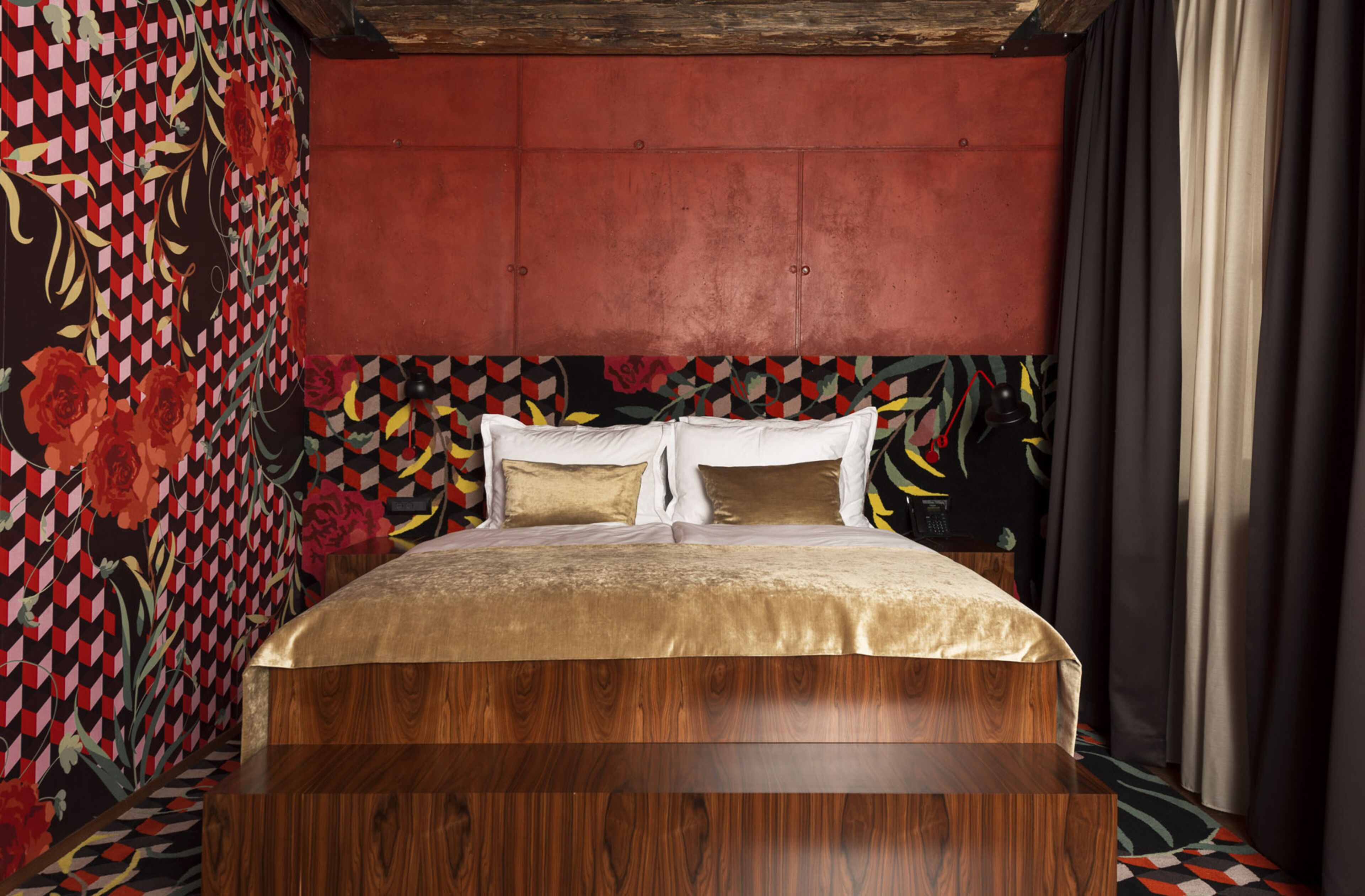 A bedroom with a wooden headboard, a bed with white and gold bedding, and a patterned wall.
