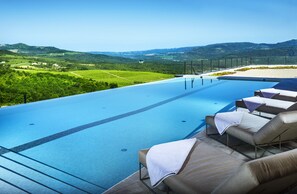 Zona de piscina con sillones de descanso y vistas a colinas verdes.