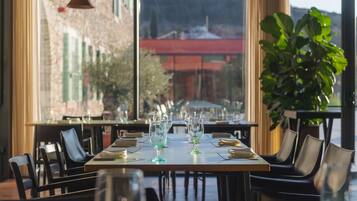 Un restaurante con una larga mesa dispuesta para comer, ventanas amplias y vistas a un edificio al fondo.