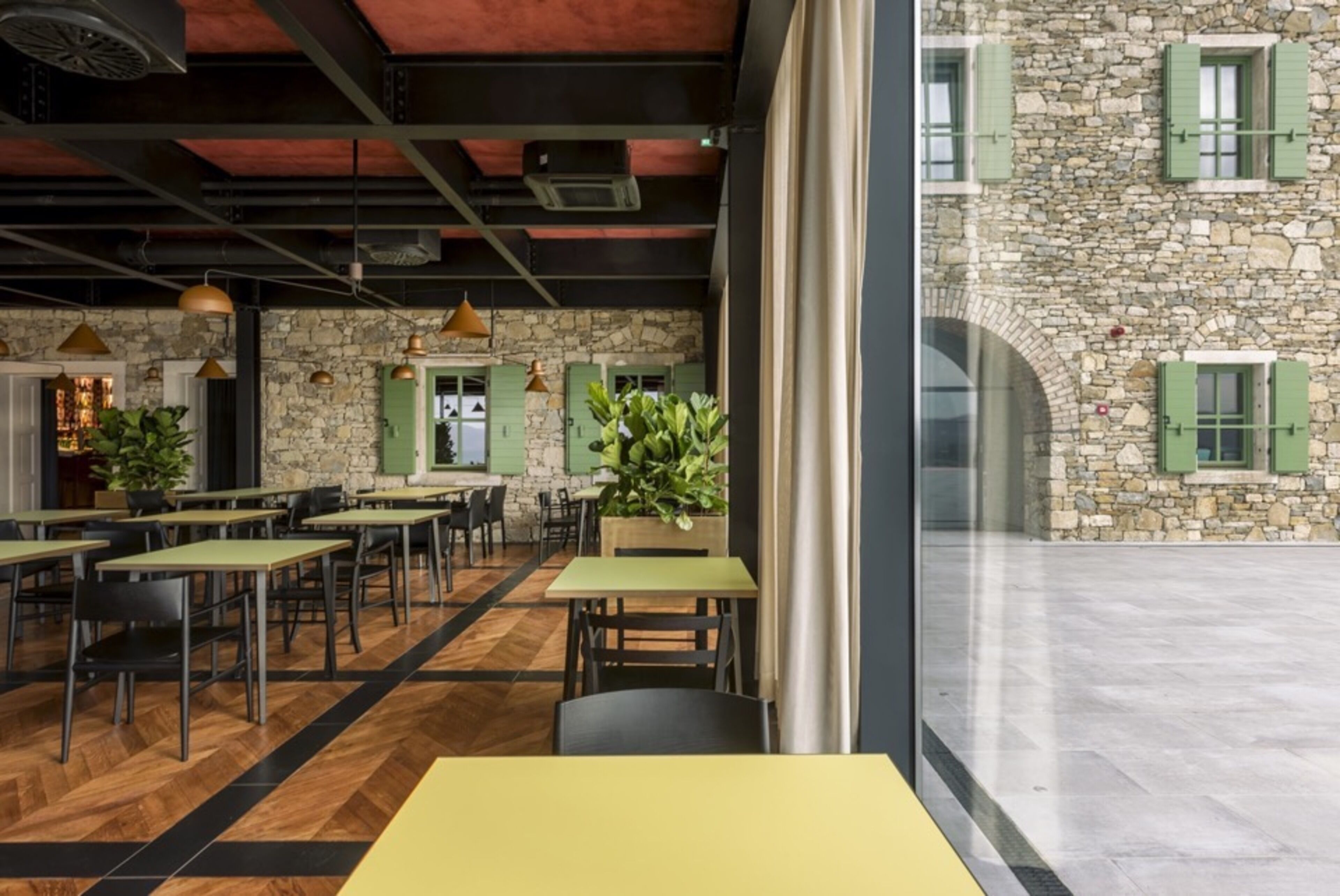 An indoor dining area with tables and chairs, a stone wall, and a view of a courtyard.