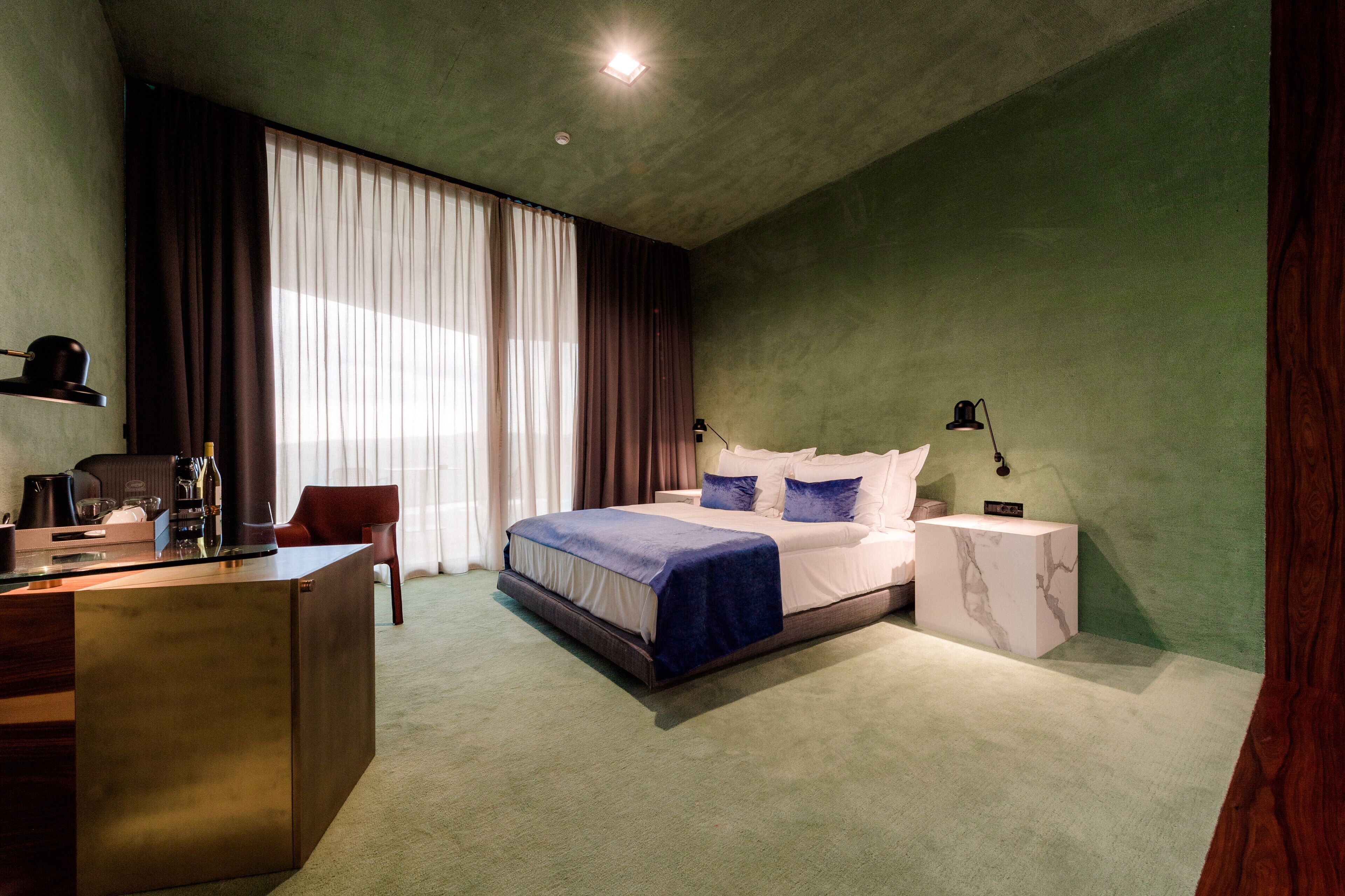 Une chambre à coucher comprenant un lit, une table de chevet, une lampe, un bureau, une chaise et des rideaux.