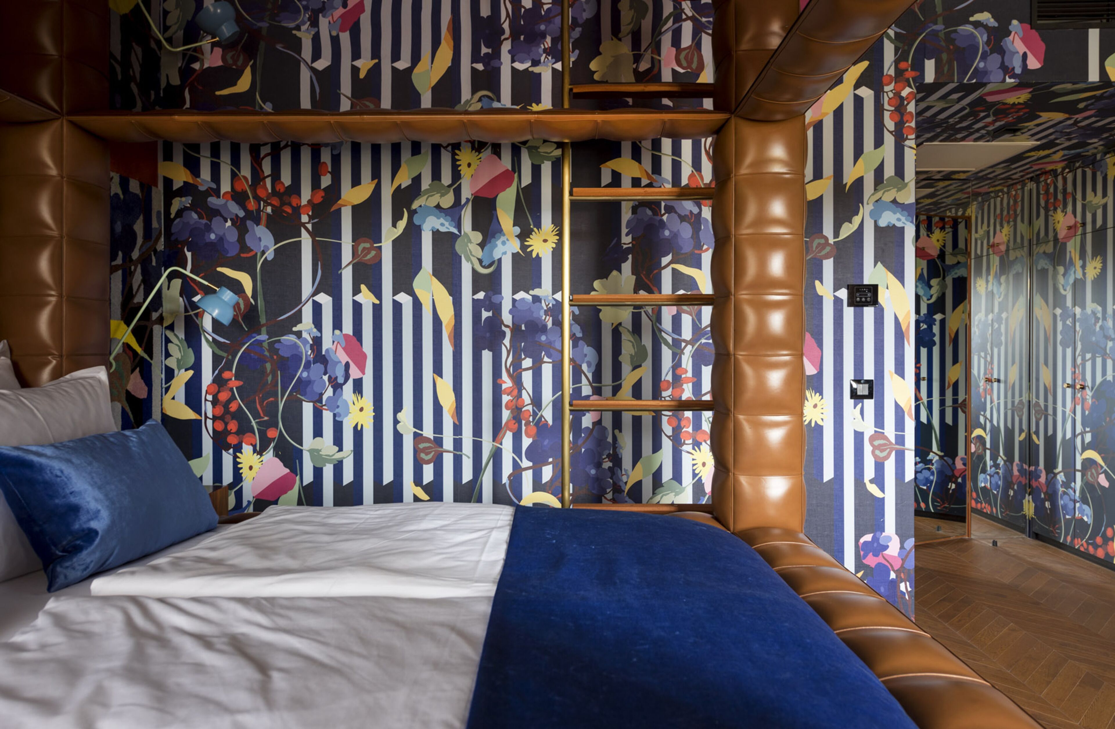 A bedroom with a bed, pillows, a blue blanket, and a wall with a floral pattern.