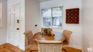 A dining area with a round wooden table, woven chairs, a decorative centerpiece, and a window with blinds.