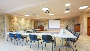Un salón de conferencias con una larga mesa, sillas, una pantalla de proyector y paredes de piedra.