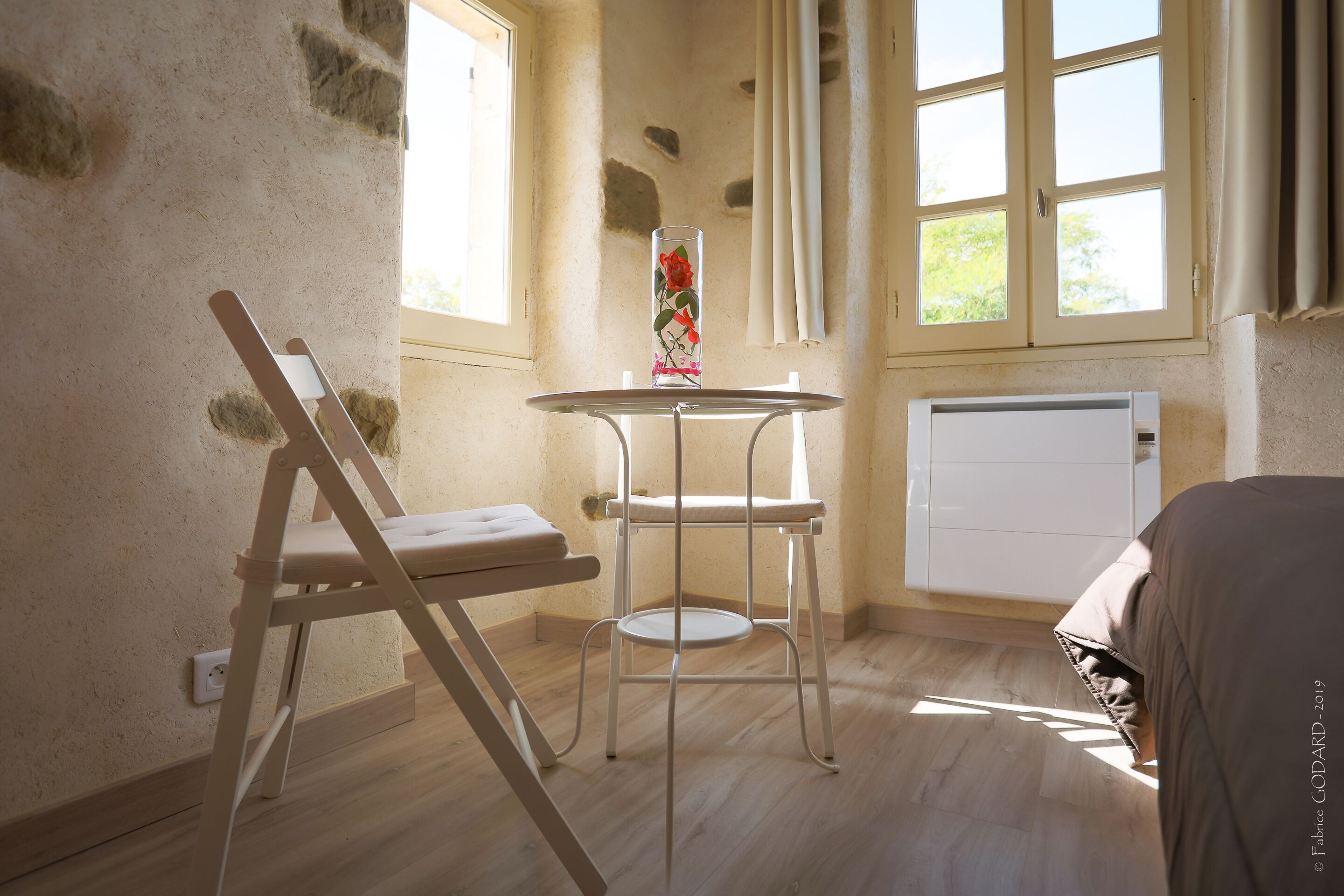 A room with a wooden floor, a white radiator, a white chair, a small table, and a window with curtains.