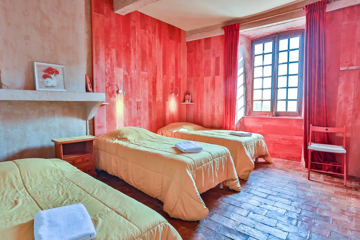 A room with two beds, a shelf with a picture, a window with curtains, and a wooden floor.