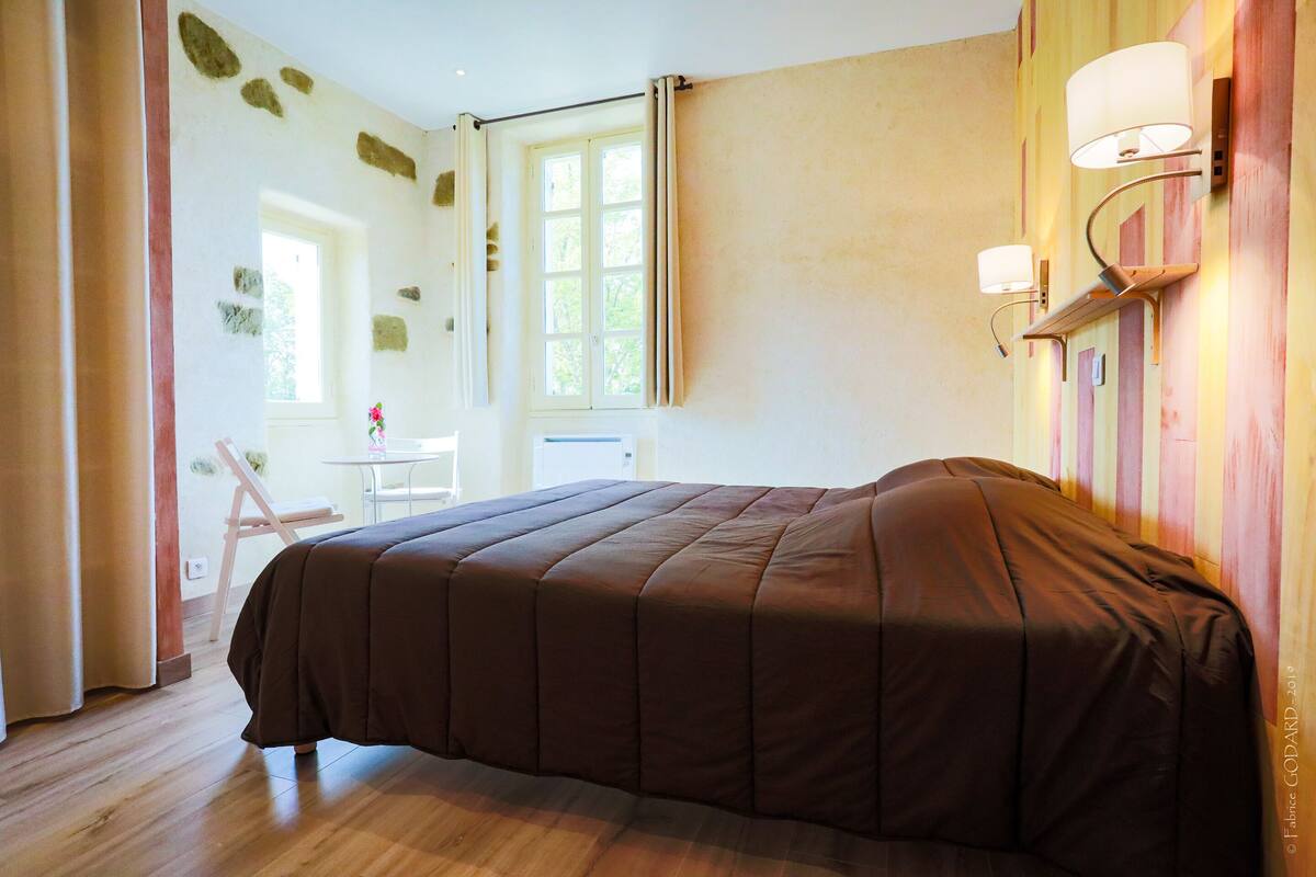 A bedroom with a large bed, a window with curtains, and wall-mounted lamps.
