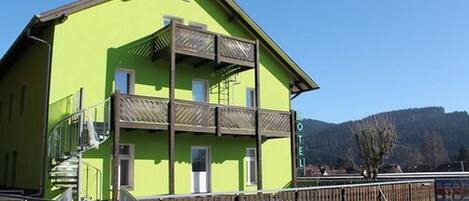 A green hotel with a balcony and a staircase leading to the entrance.