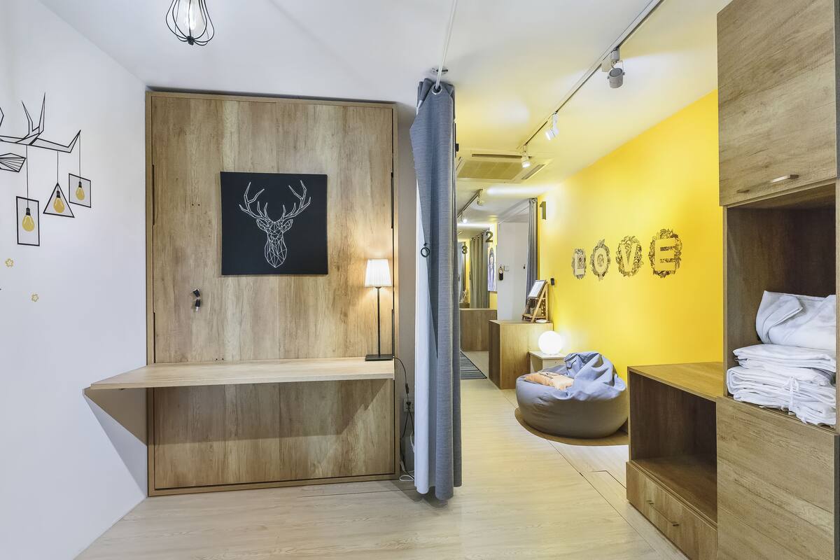 Une chambre d’hôtel moderne avec un comptoir d’accueil en bois, une décoration murale représentant une tête de cerf, un mur d  ’accent jaune vif et un coin salon bien aménagé avec une lampe.