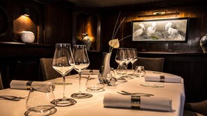 Una mesa de comedor dispuesta con copas de vino, platos y cubiertos, con un jarrón y un cuadro en la pared.