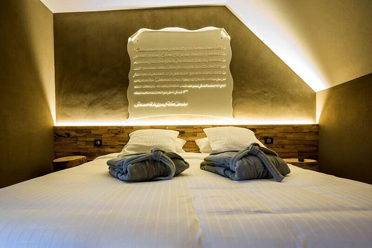 Quarto de hotel com uma cama grande, duas almofadas e uma luminária fixada na parede.