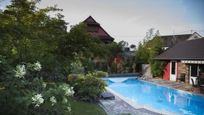 Una piscina rodeada de abundante vegetación y un edificio con techo rojo.