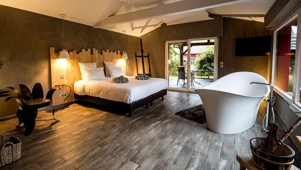 Un dormitorio moderno con una cama grande, una bañera independiente y un ventanal corredero que da a un balcón.