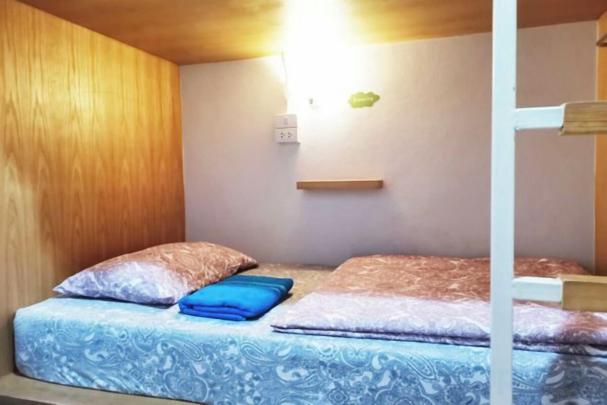 A bunk bed with a patterned bedspread, a wooden wall, and a small shelf with a light fixture.