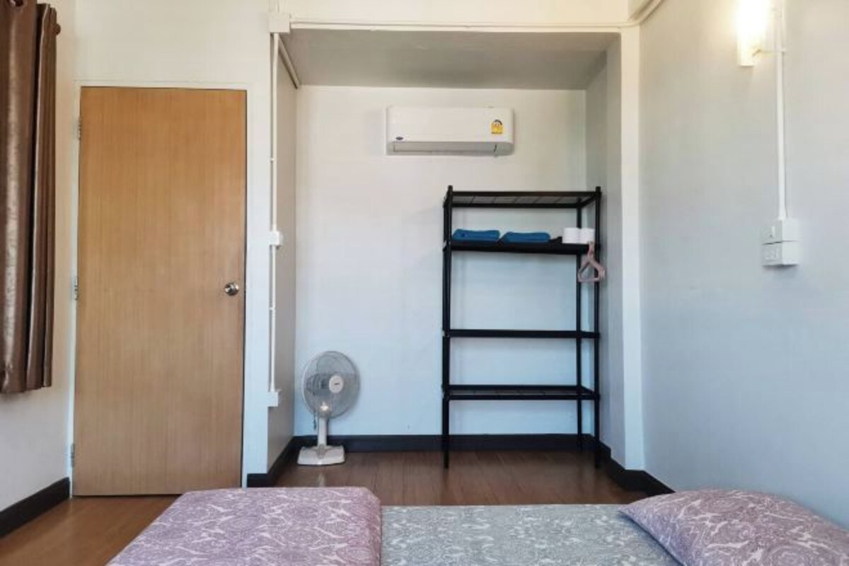 A small, compact room with a bunk bed, a standing fan, and an air conditioning unit on the wall.