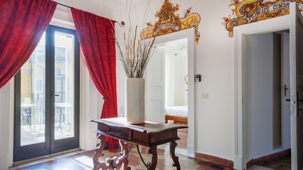 Quarto com uma mesa de madeira, um vaso com galhos, cortinas vermelhas e um espelho grande.