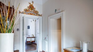 A hallway with a tiled floor, a white door, a wooden table with a glass pitcher, and a decorative sign above the door. - Francalanza City Rooms (Catania)