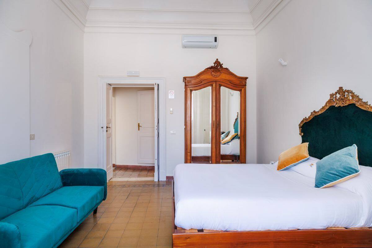 A bedroom with a bed, a wardrobe, and a teal sofa.
