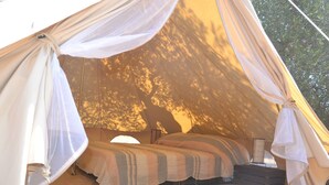 A tent with a bed, a small table, and a red rug. - Accampamento Rurale Macaria (Alliste)