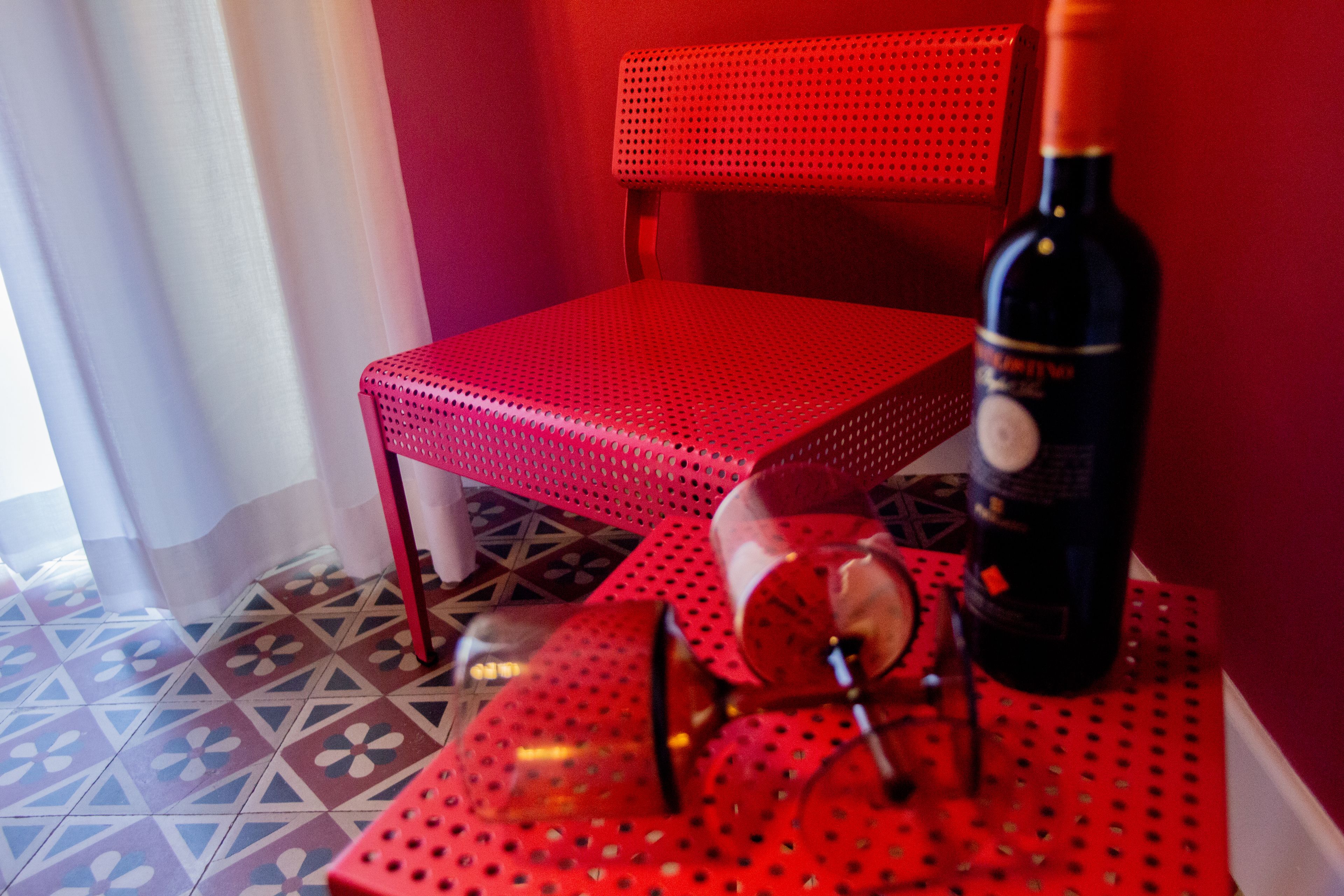 A red chair, a table, and a bottle of wine on a patterned floor.