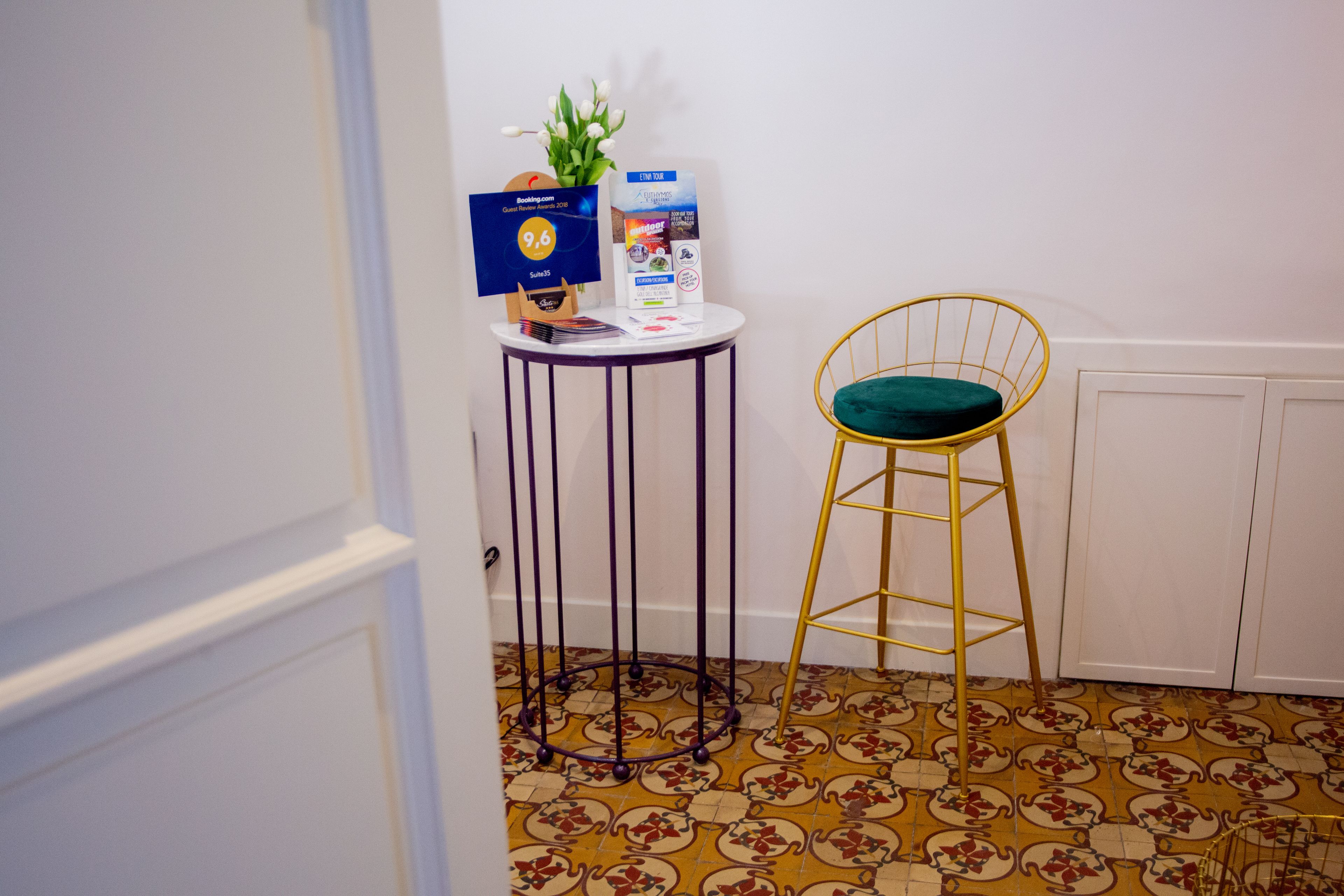 A small room with a patterned floor, a round table with a blue sign, a yellow chair, and a white cabinet.