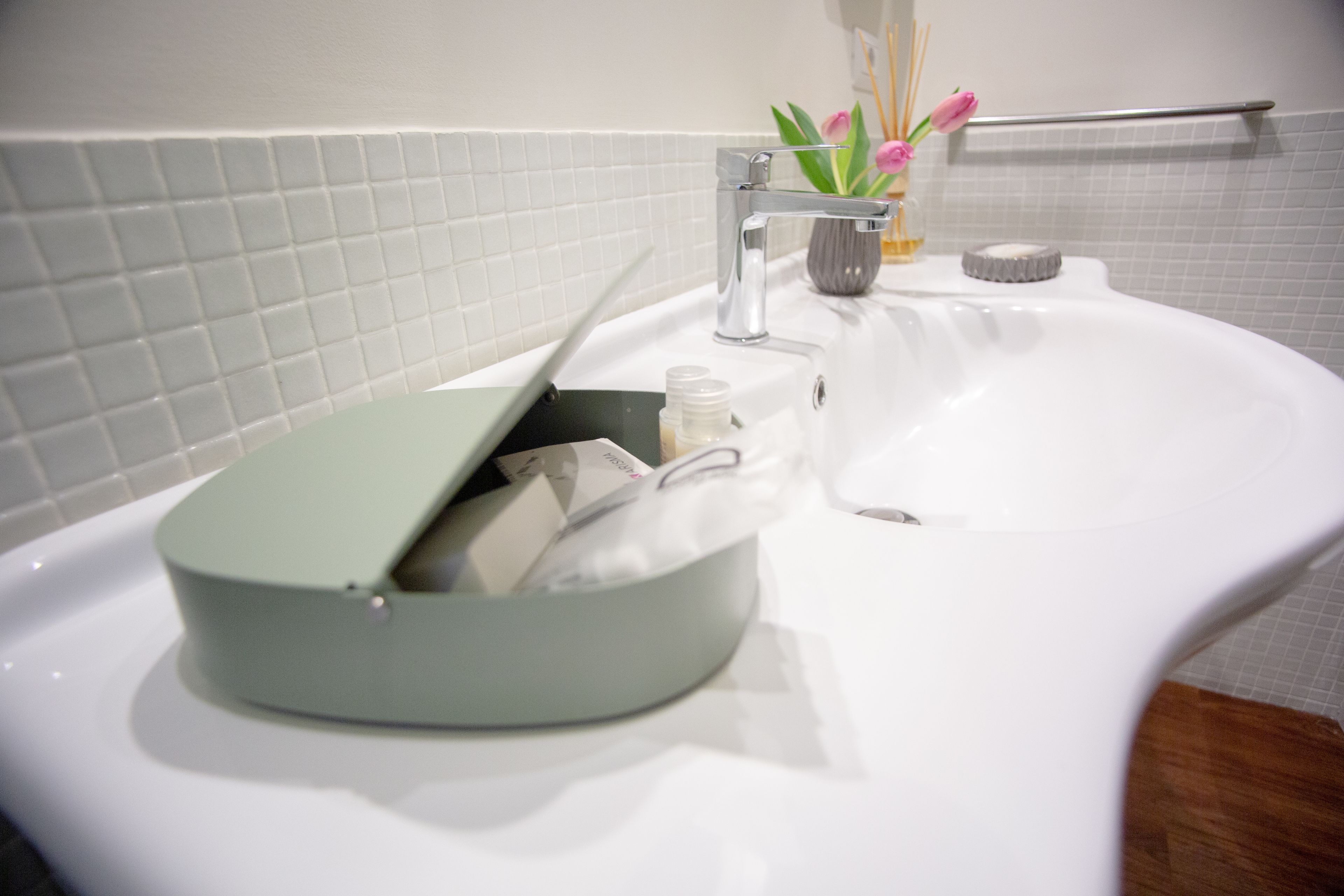 Un lavabo de bany amb un plat per sabó verd, una tovallola blanca i un vas petit amb flors.