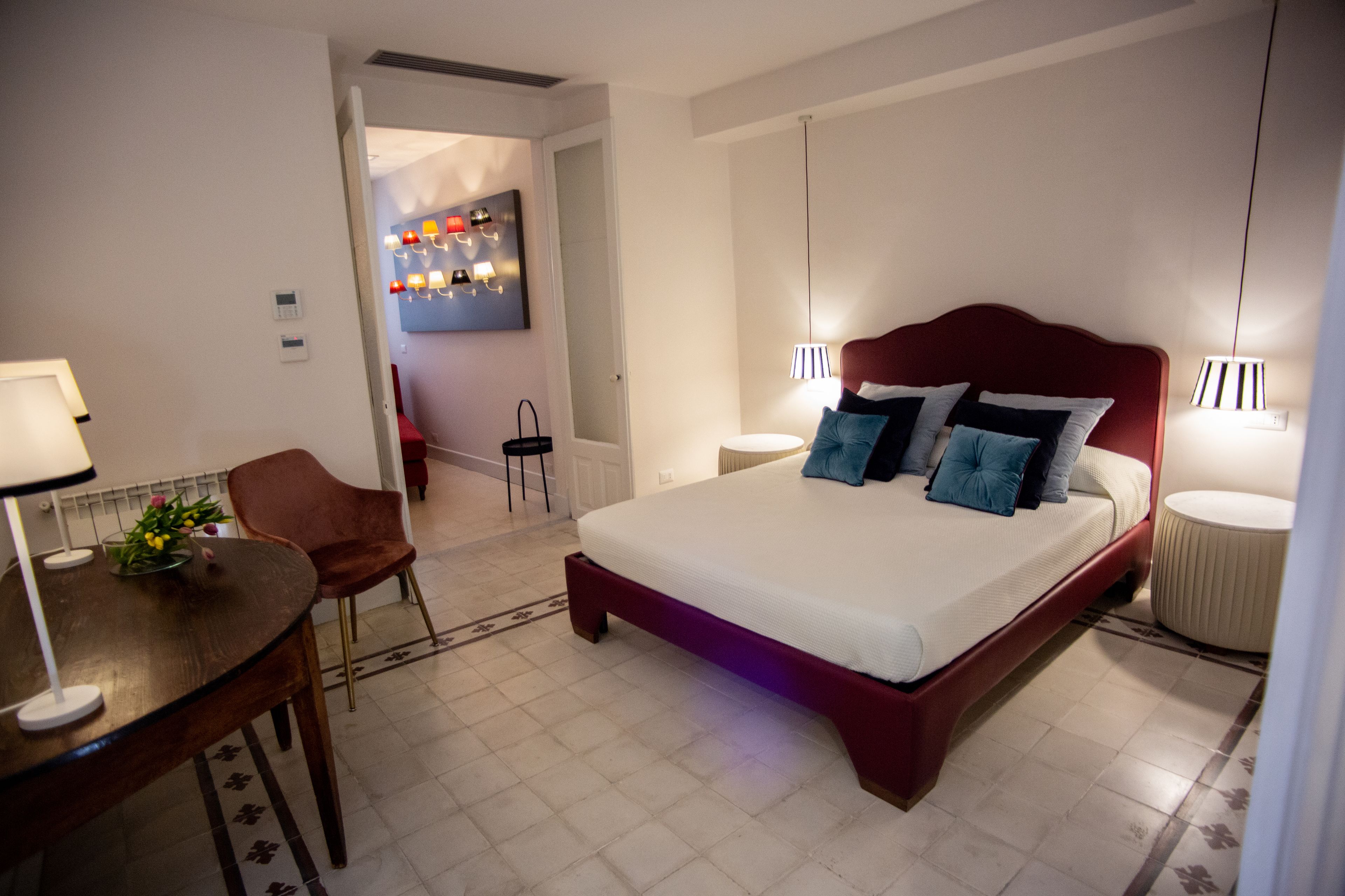 Habitación de hotel con una cama grande, un escritorio con lámpara, una silla y una mesita con flores.