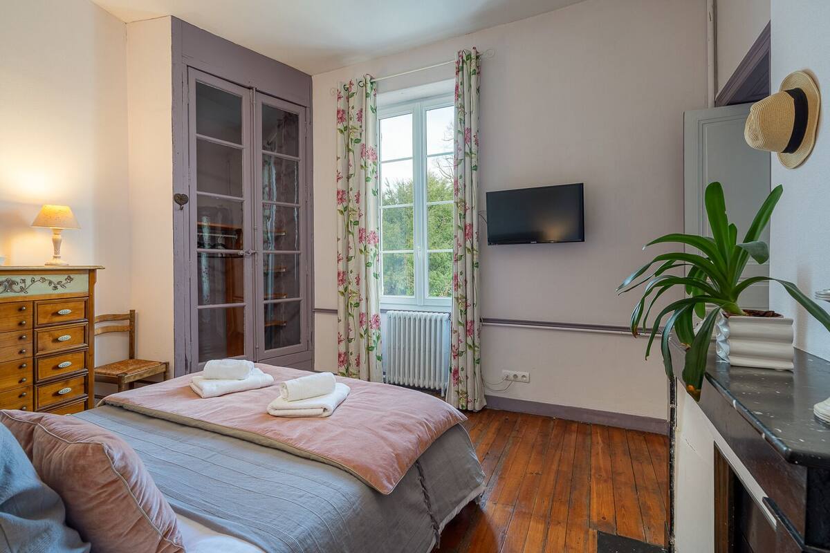 A bedroom with a bed, a dresser, a TV, and a window with curtains.