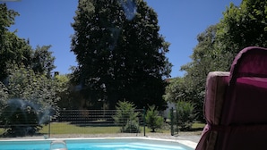 A poolside area with a glass of drink, a chair, and a view of a tree and fence. - Chambres d'hôtes H De Surgeres (Surgeres)