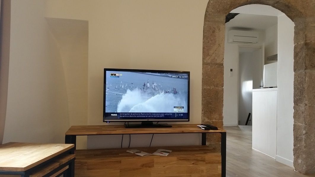Un televisor sobre un atril de madera en una habitación con un arco de piedra y una pared blanca.