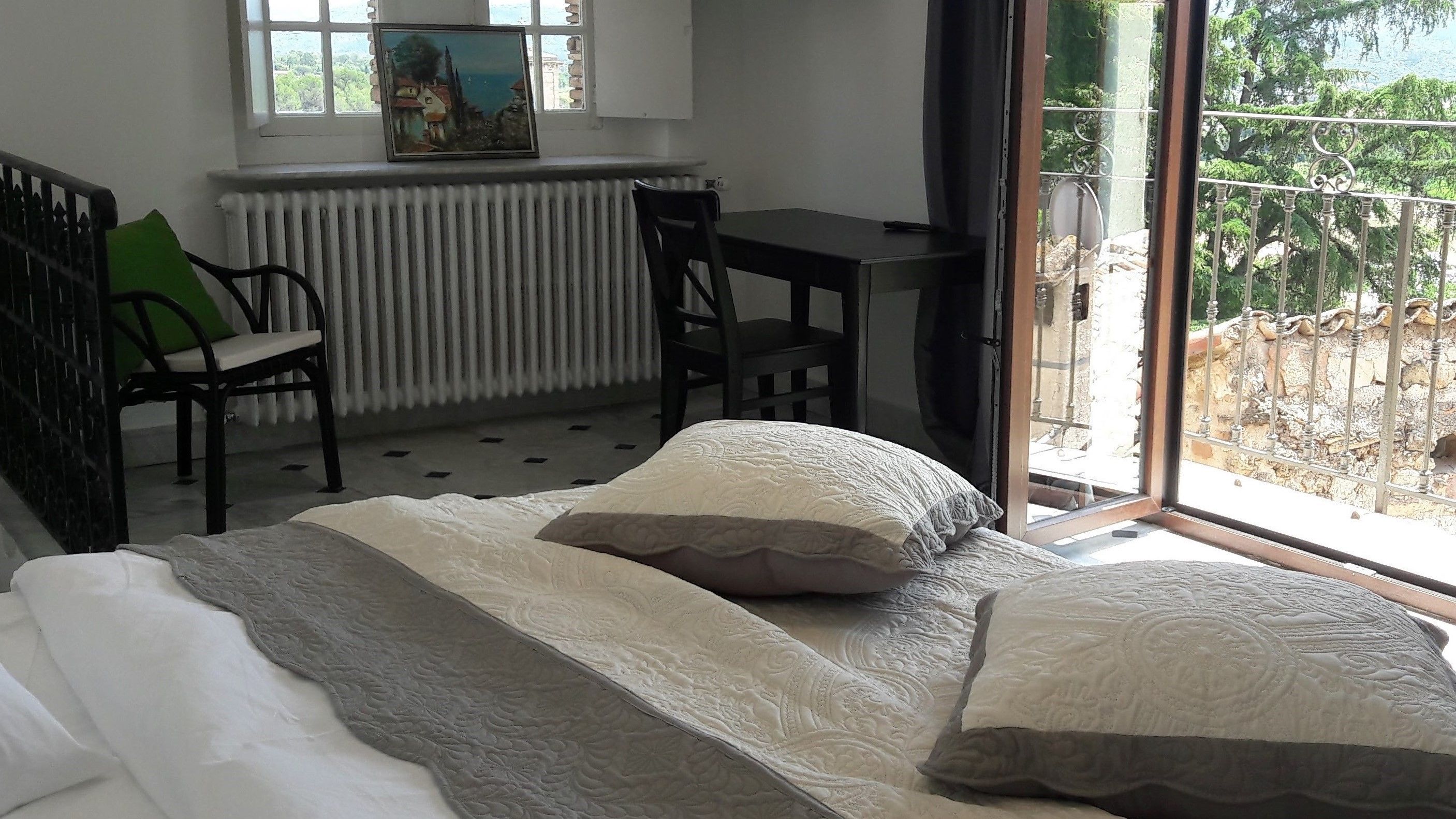 A bedroom with a bed, a chair, a table, and a window with a view of greenery.