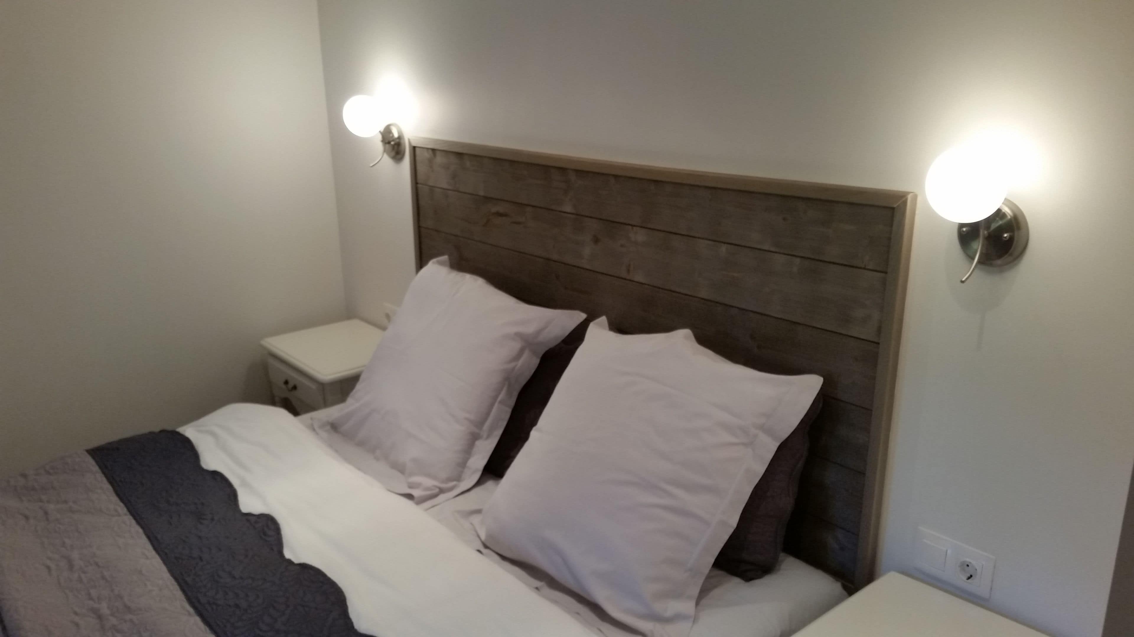 Una cama con cabecera de madera, dos mesitas de noche y lámparas fijadas a la pared.