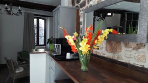 Una cocina con pared de piedra, encimera de madera, una cafetera y un florero con flores.